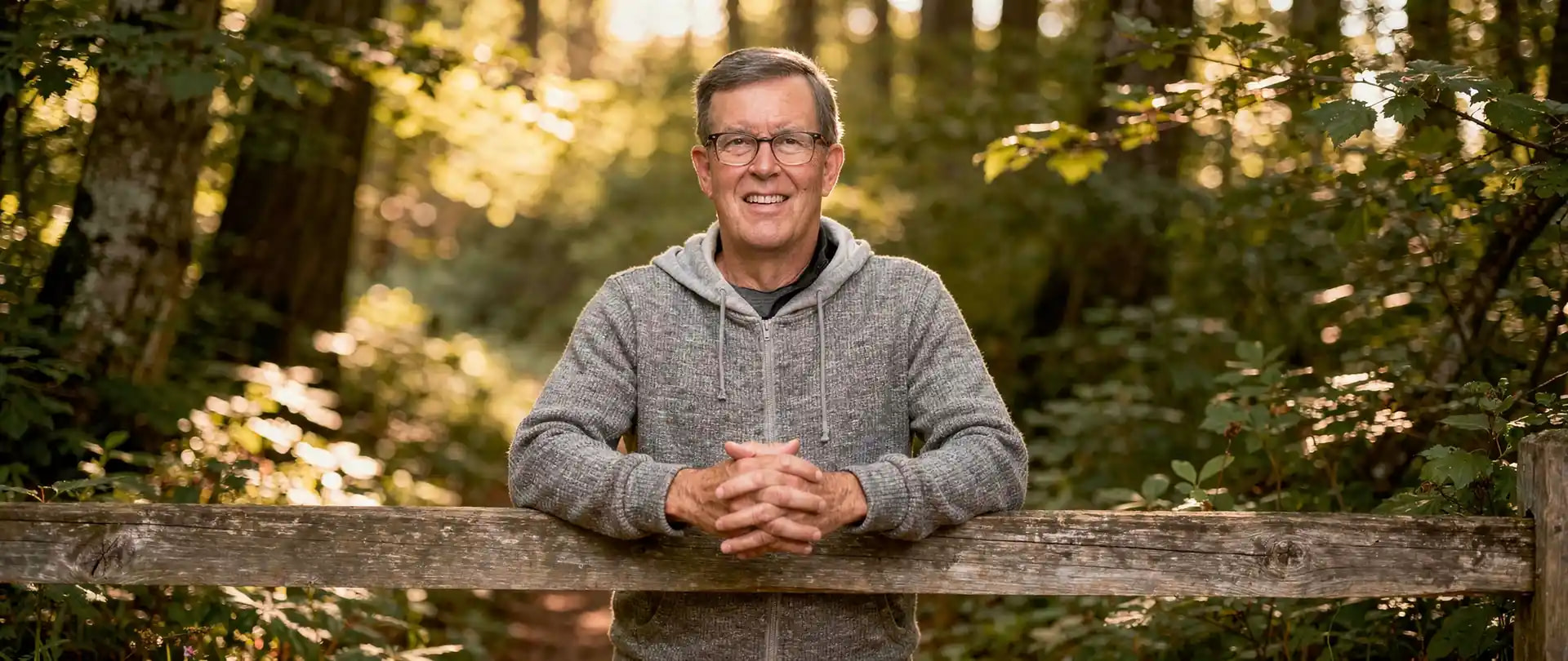 Image of Michael Christian leaning on split rail fence in a forest